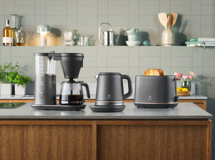 Blat kuchenny z ekspresem do kawy, czajnikiem i tosterem. Wszystkie czarne urządzenia i drewniany blat.