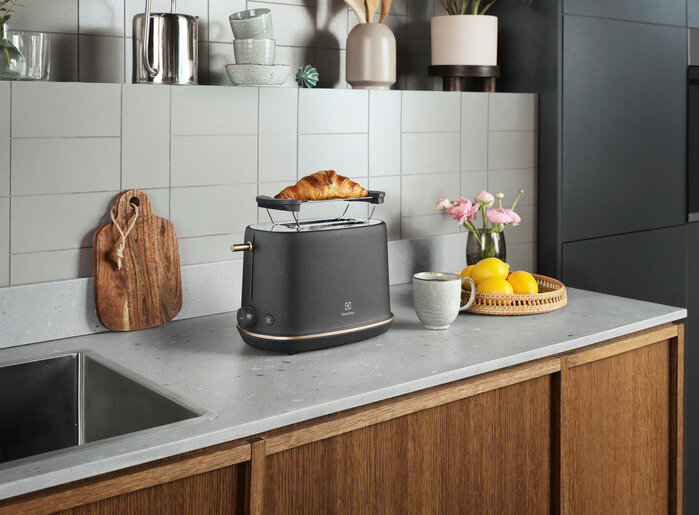 Czarny toster z rogalikiem na wierzchu. Kuchnia ma drewniany blat i okno.