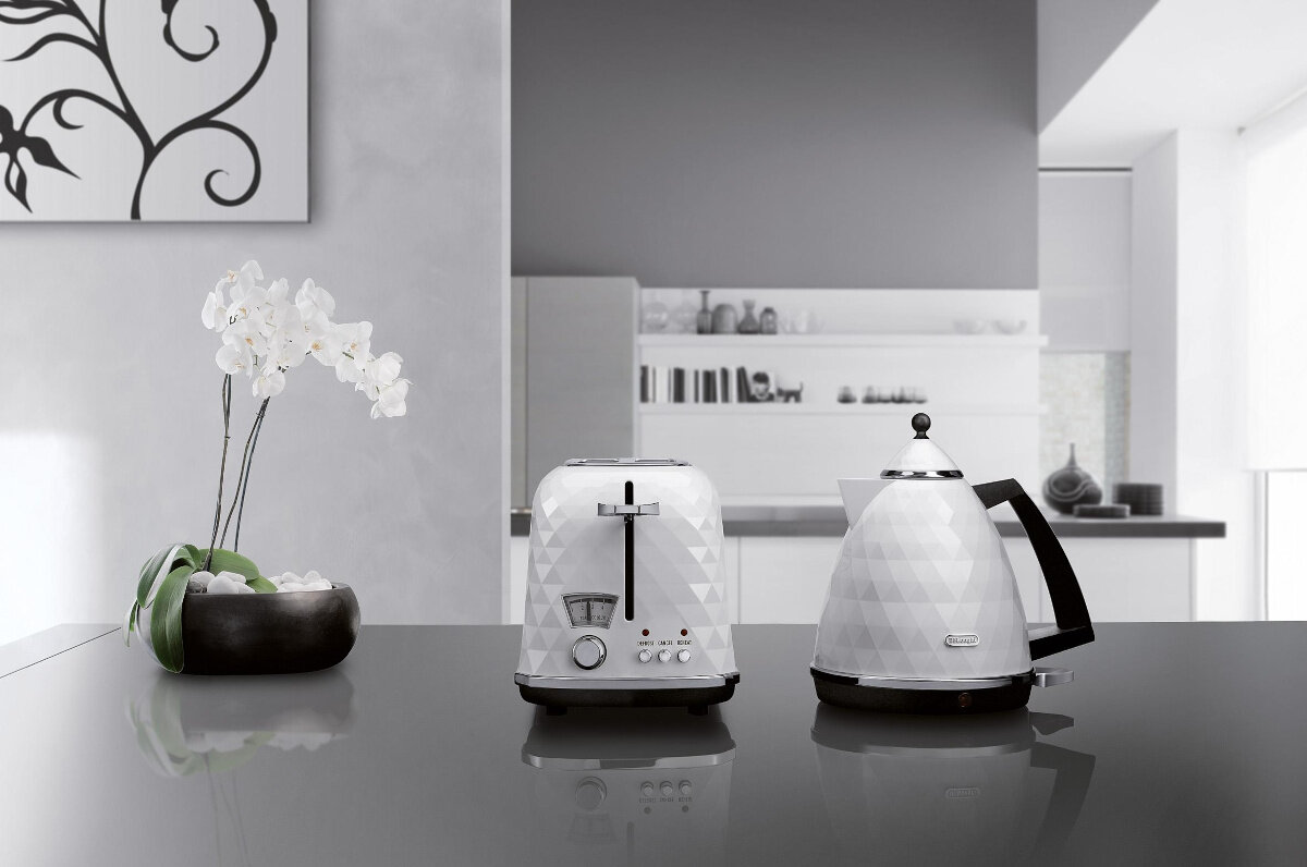 Scena kuchenna z białymi urządzeniami, kwiatami i ciemnym blatem.