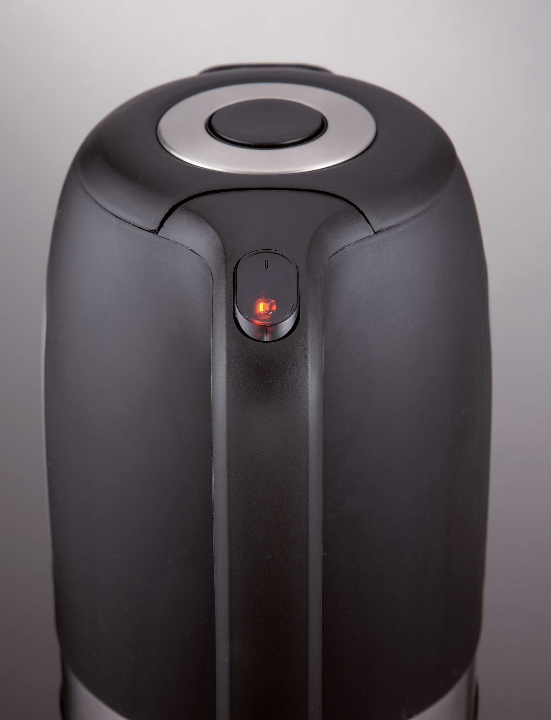 Czarny czajnik z zapalonym czerwonym światełkiem. Zbliżenie, czarny ze srebrnymi akcentami. Szare tło.