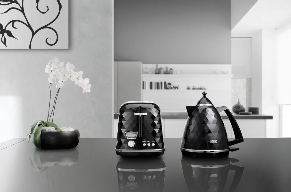Czarny toster i czajnik z diamentowym wzorem na szarym blacie, z wazonem z kwiatami.