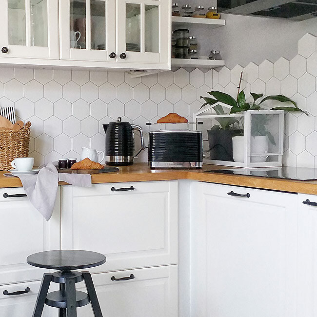 Kuchnia z białymi szafkami, drewnianym blatem, sprzętem i roślinami.