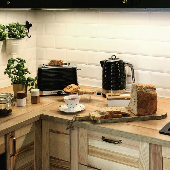 Blat kuchenny z tosterem, czajnikiem i chlebem. Biała ściana z kafelkami i drewniany blat.