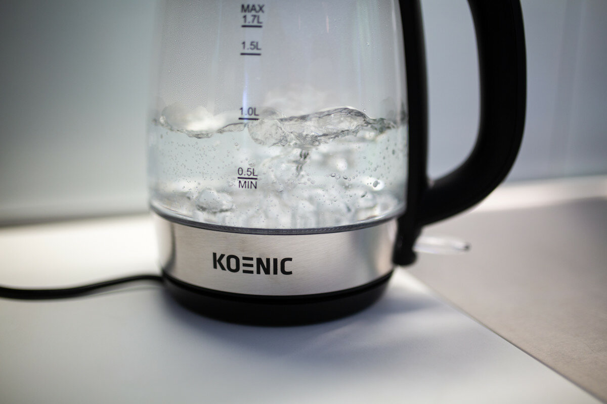 Czajnik elektryczny Koenic z wrzącą wodą w środku, na białym blacie.