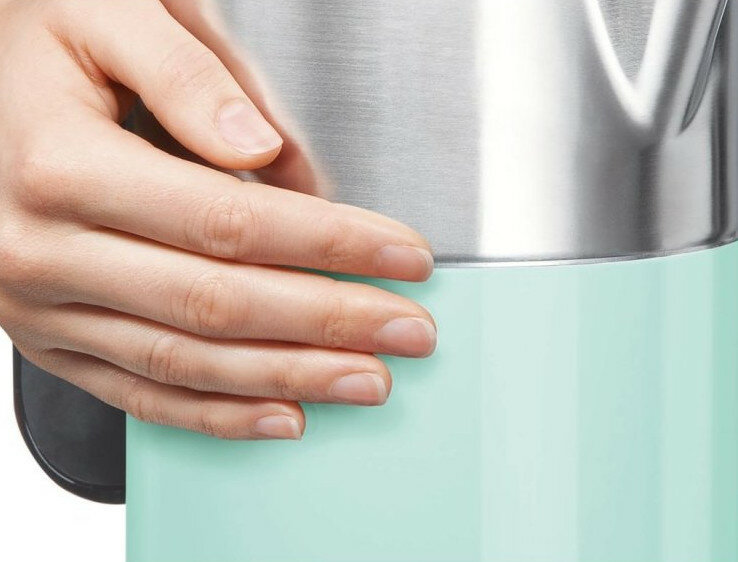 Ręka trzymająca turkusowy czajnik elektryczny, zbliżenie, fokus na uchwycie.