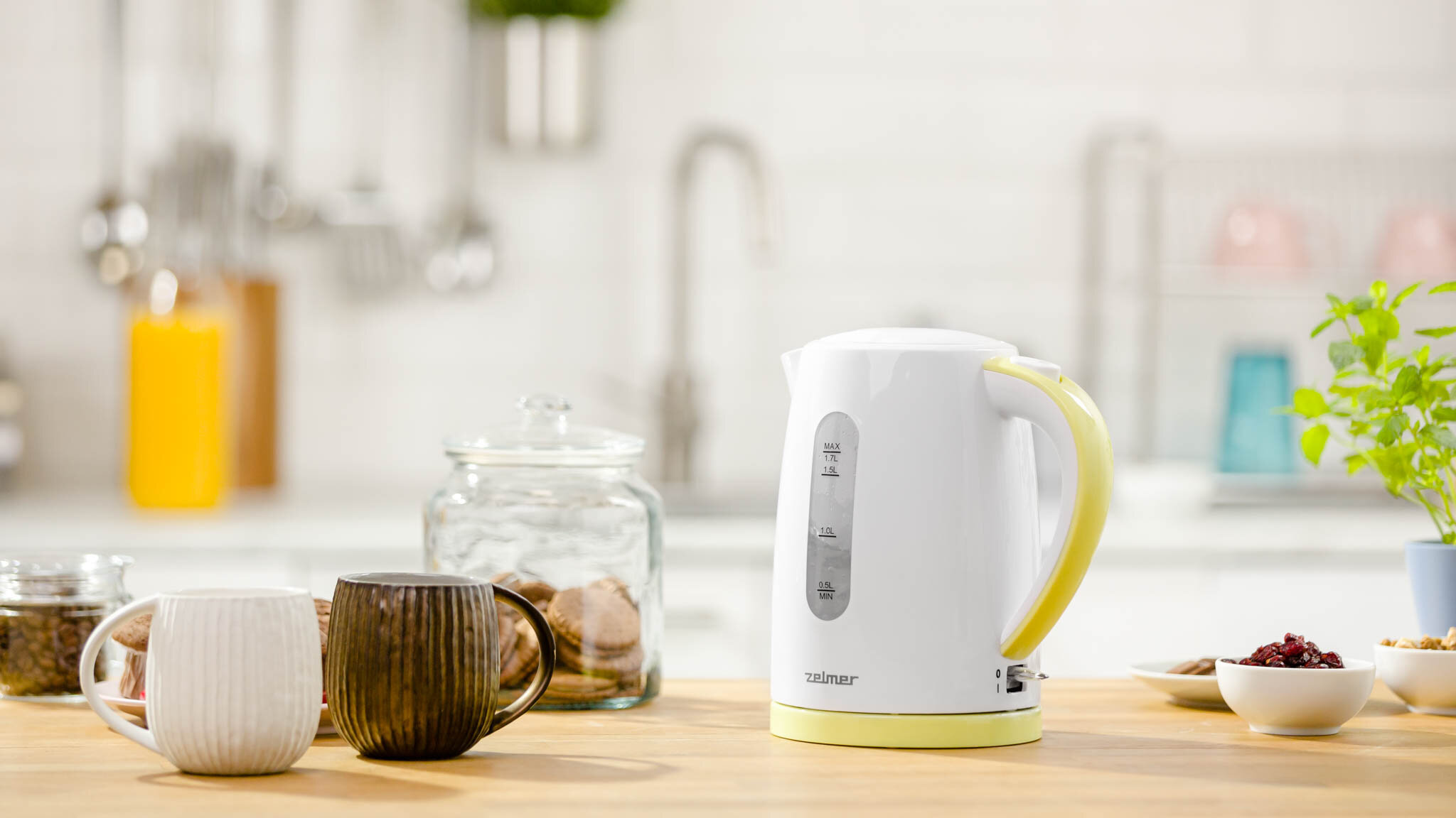 Biały czajnik elektryczny z żółtym uchwytem stoi na drewnianym stole.