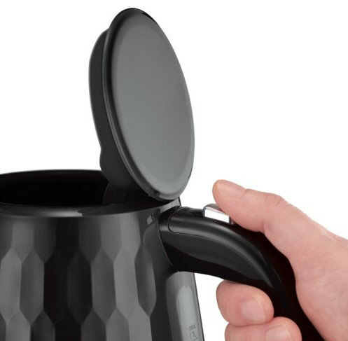 Zbliżenie dłoni otwierającej pokrywę czarnego czajnika elektrycznego.