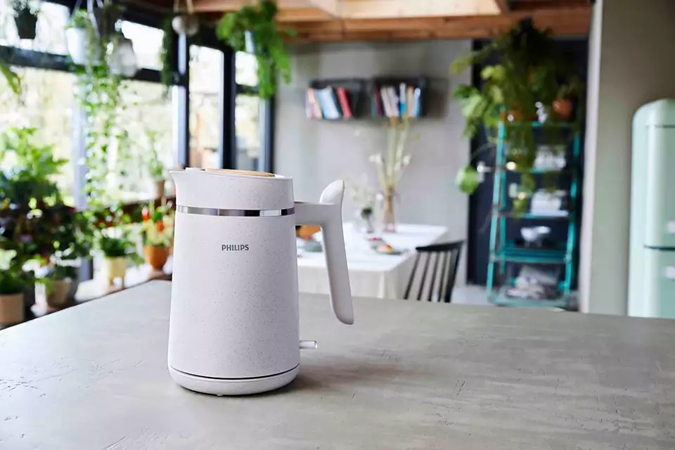 Biały czajnik Philips na blacie. Rośliny i stół jadalny w tle.