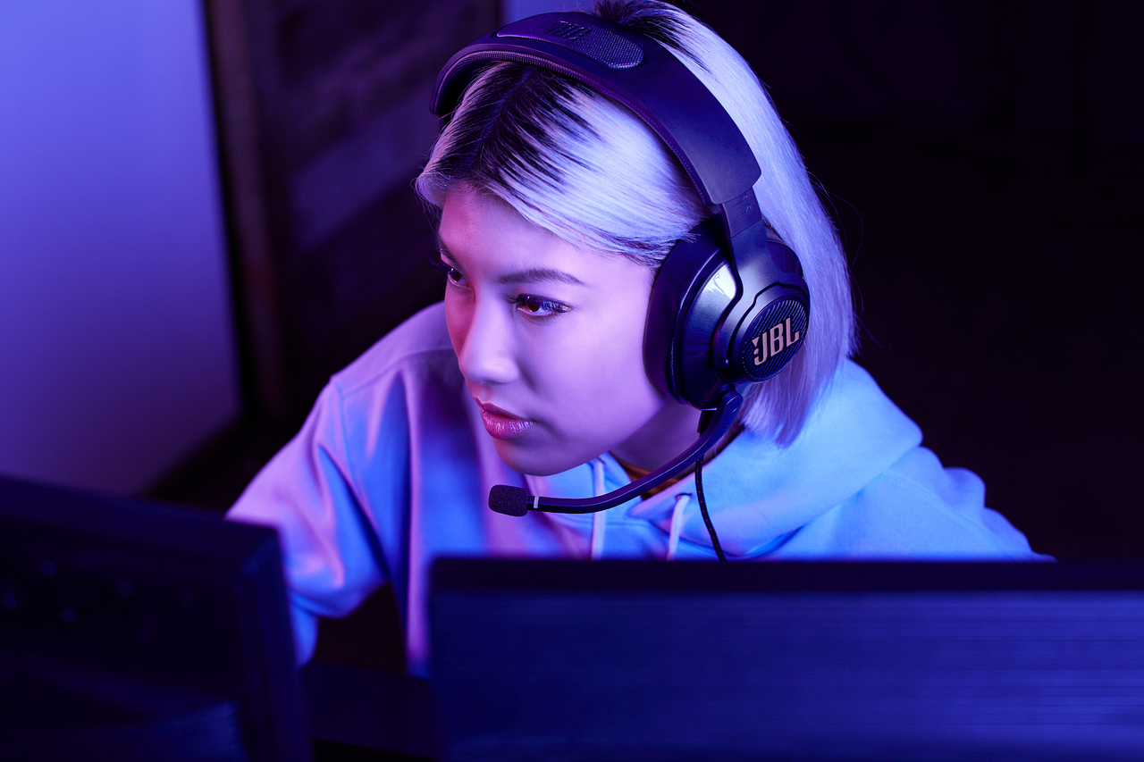 Frau mit schwarzem JBL Gaming-Headset mit Mikrofon, vor einem Computerbildschirm.