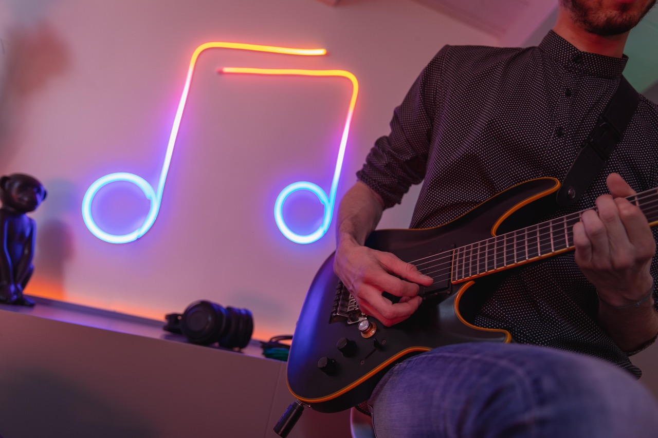 Persona che suona una chitarra elettrica davanti a una nota musicale al neon su un muro.