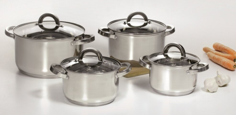 Cztery garnki ze stali nierdzewnej z pokrywkami na stole z warzywami.