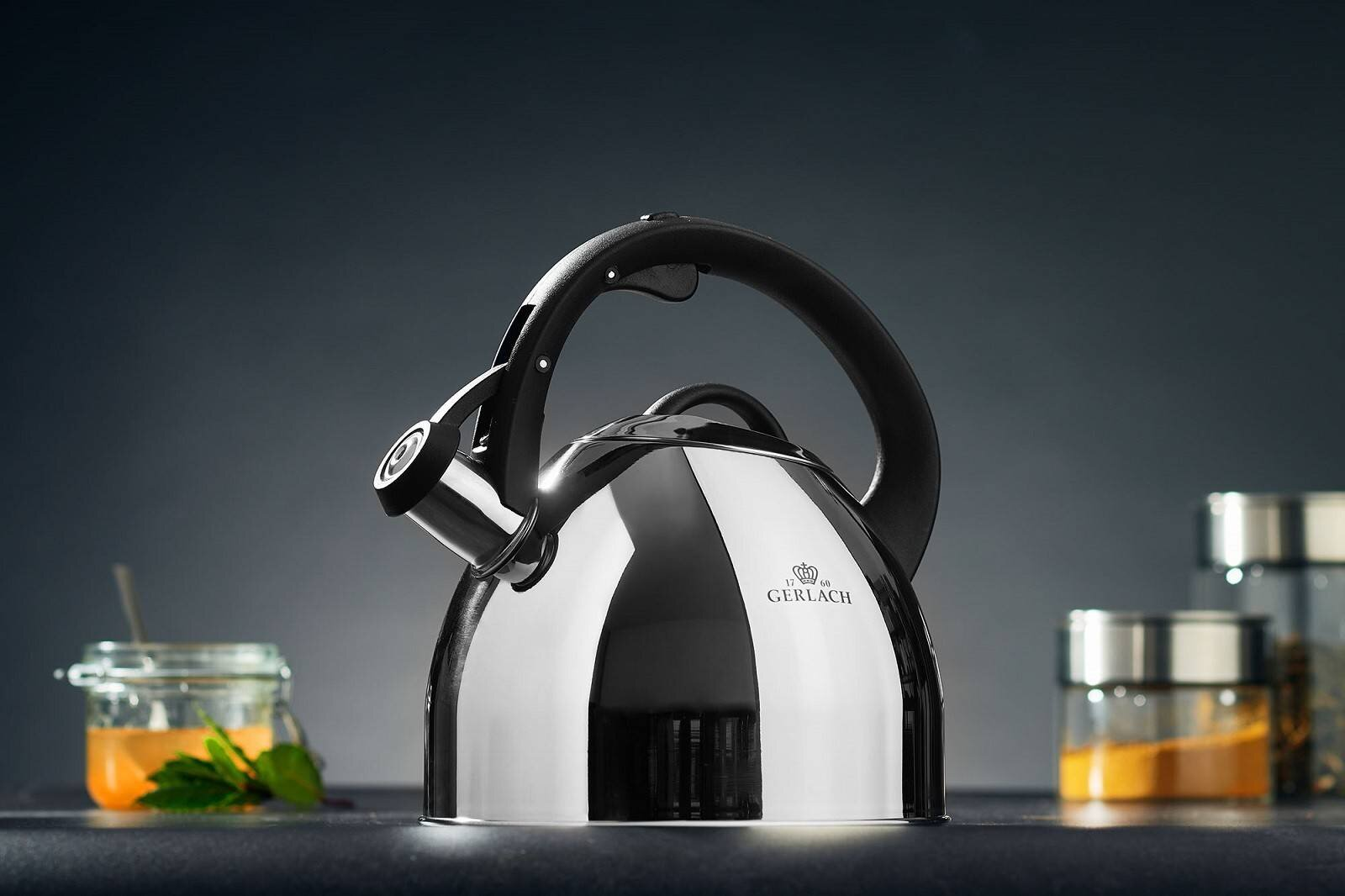 Czajnik Gerlach ze stali nierdzewnej z czarnym uchwytem. Słoiki z przyprawami i miodem w tle.