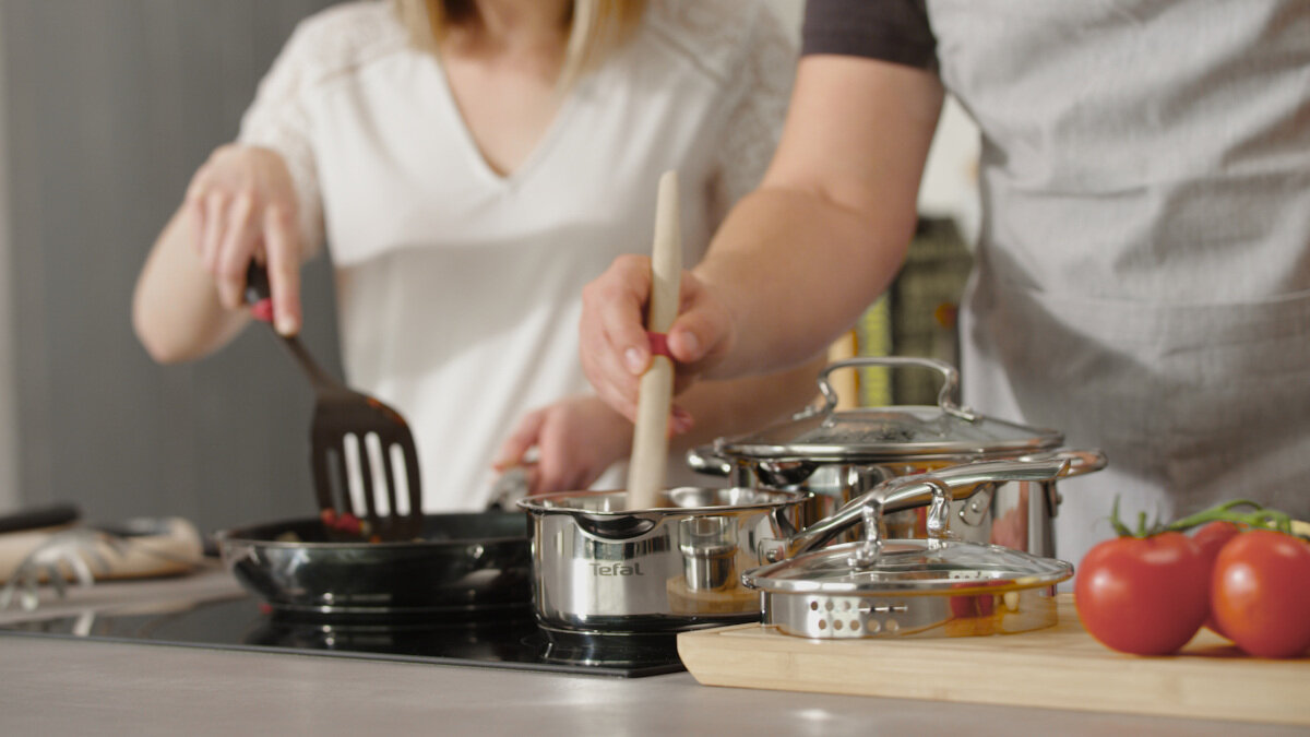 Dwie osoby gotują. Jedna miesza w patelni, druga trzyma łyżkę. Kuchnia.