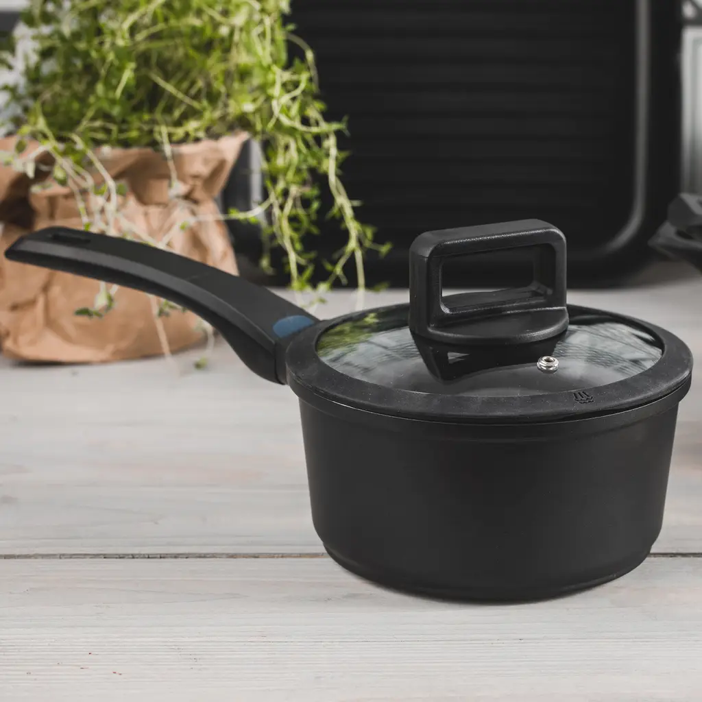 Czarny garnek ze szklaną pokrywką na drewnianym stole, tło rozmyte.