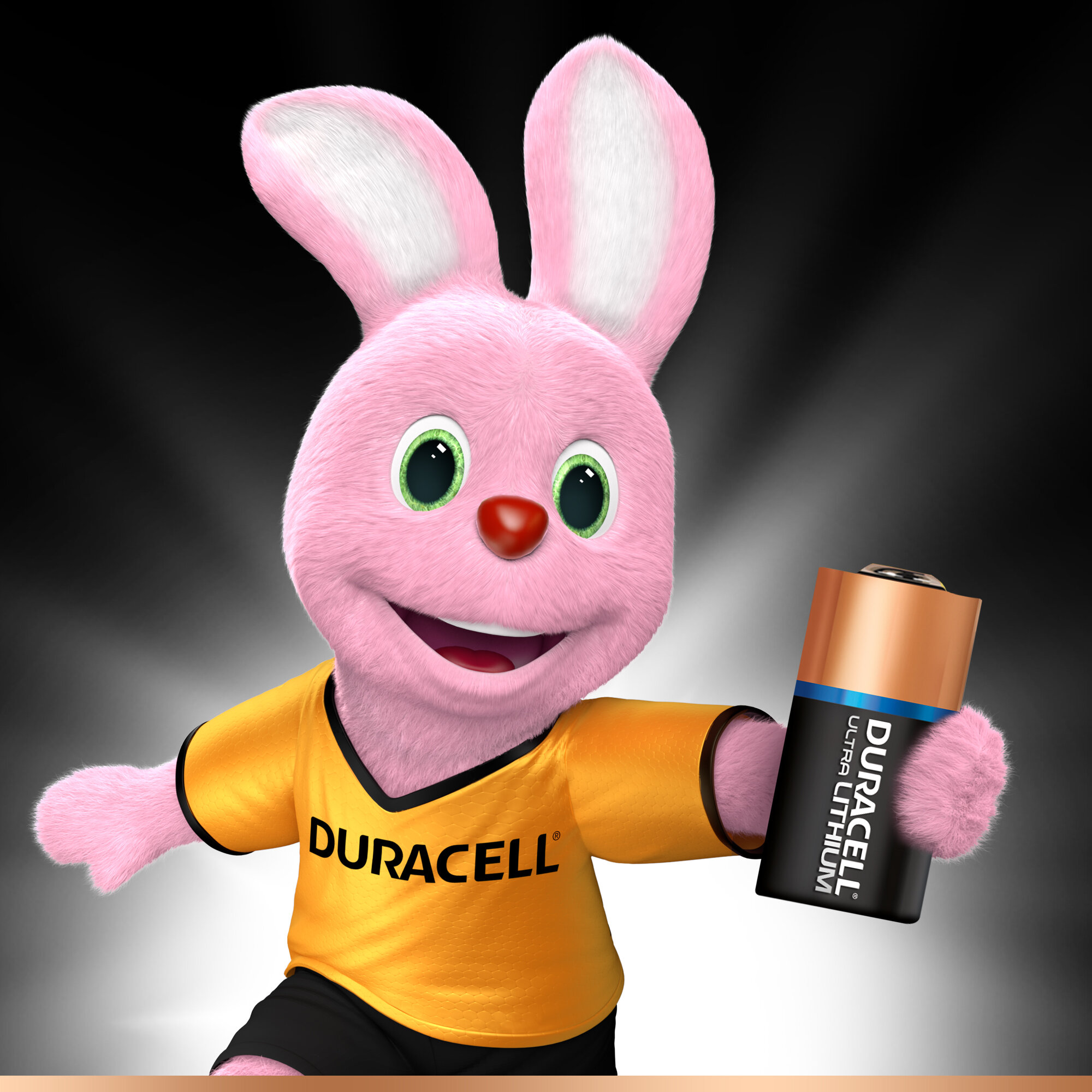 Różowy królik Duracell trzymający baterię z tekstem. Królik ma na sobie pomarańczową koszulkę i się uśmiecha.