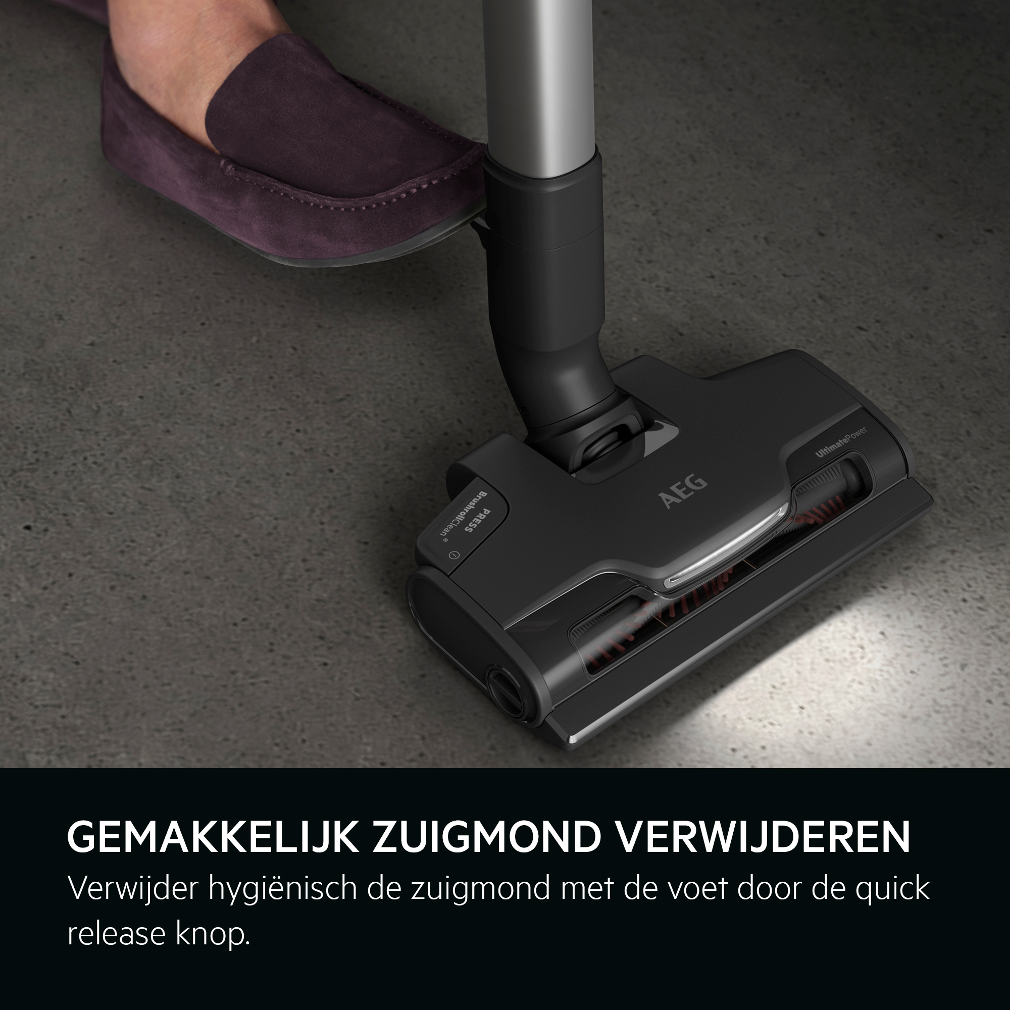 A person's foot presses the release button of a black vacuum cleaner head on a gray floor.