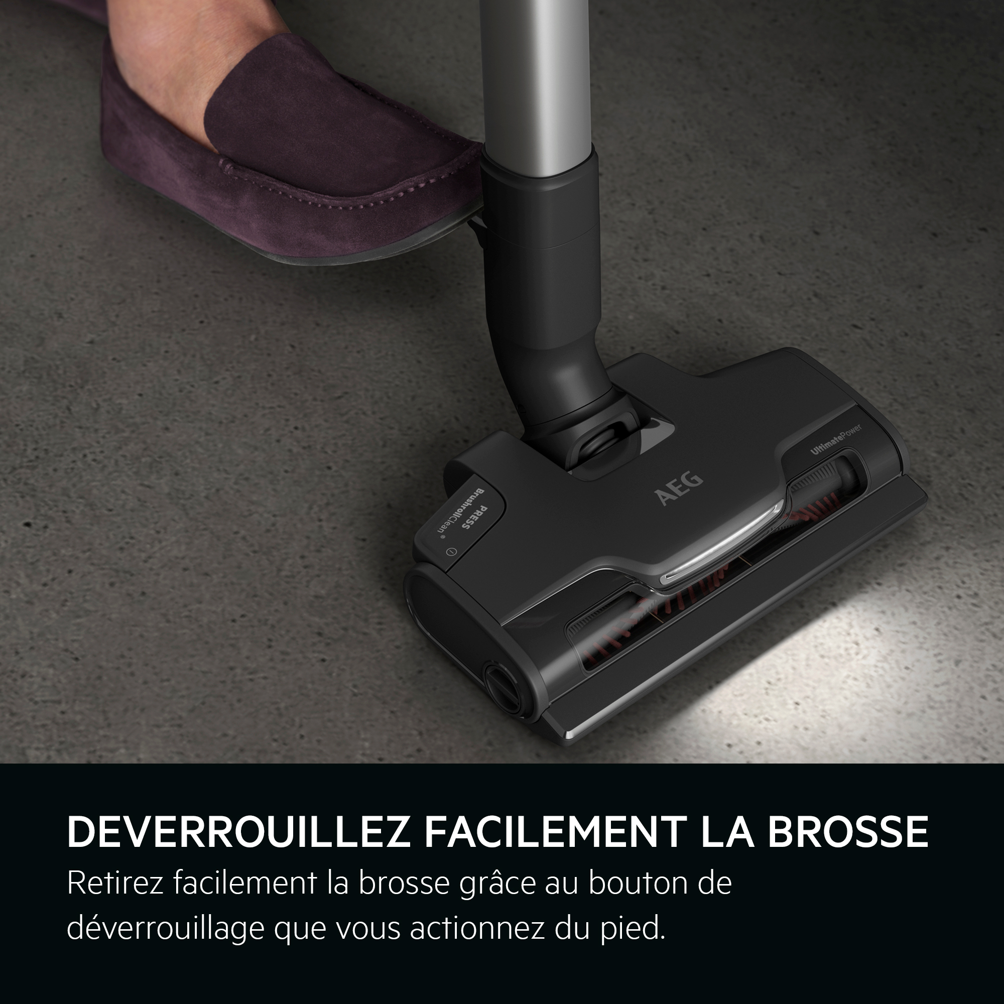 Pied d'une personne appuyant sur la tête noire de l'aspirateur, avec le logo AEG.