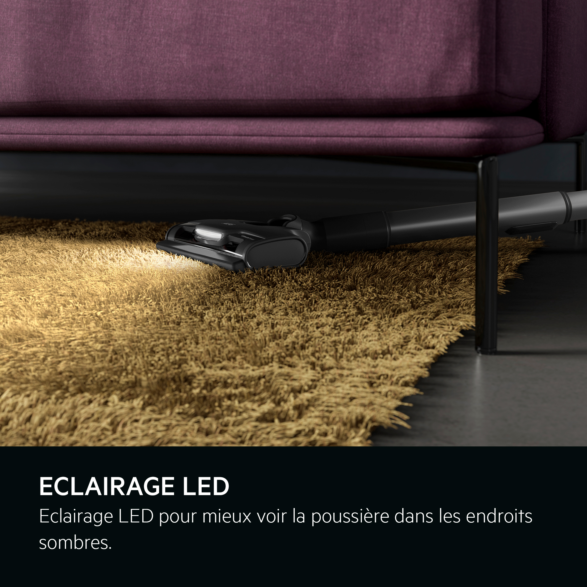 Une tête d'aspirateur sous un canapé. Un faisceau de lumière illumine le tapis, mettant en valeur l'éclairage LED.