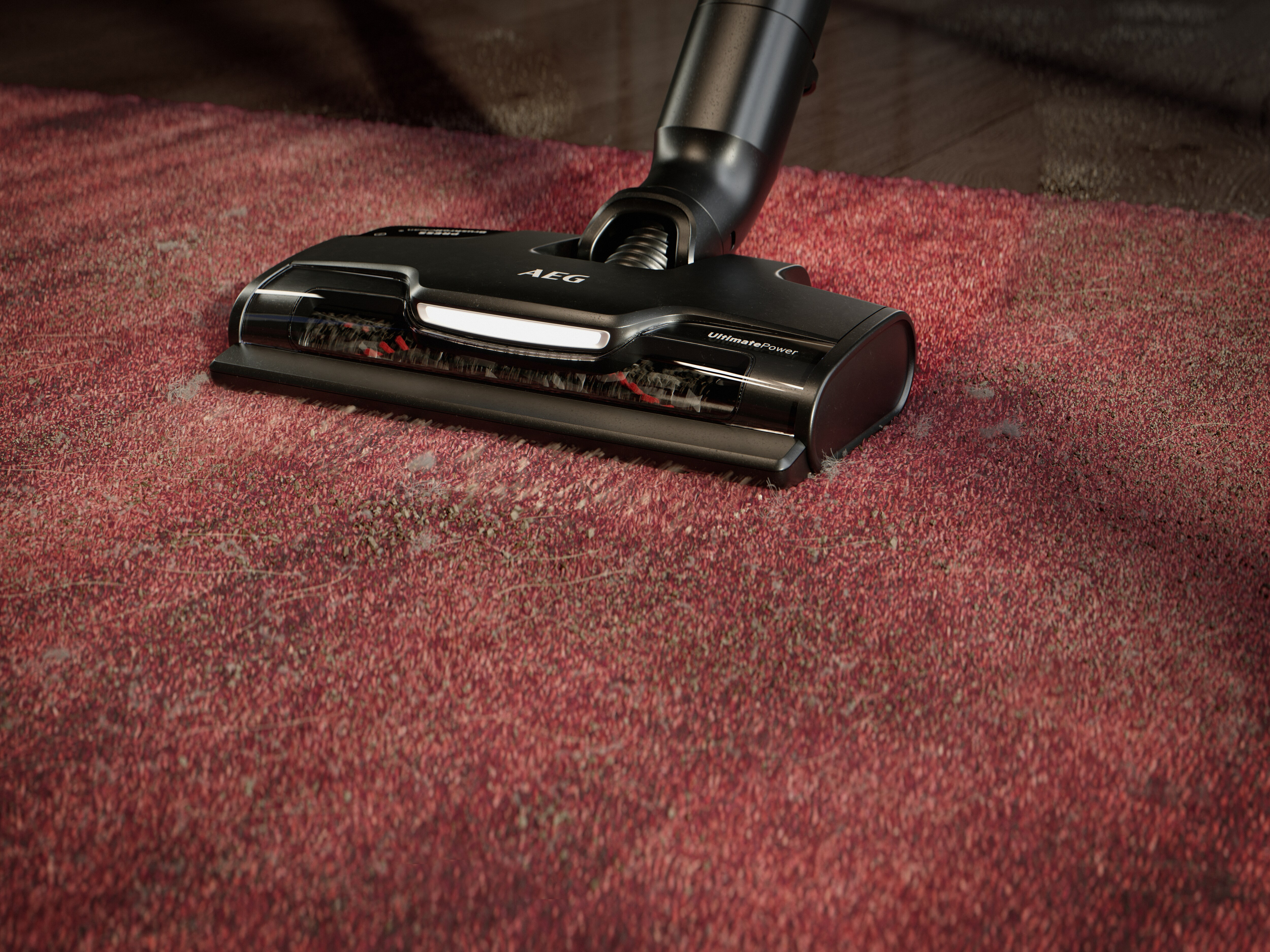Close-up of a vacuum cleaner head on a red carpet, AEG brand visible.