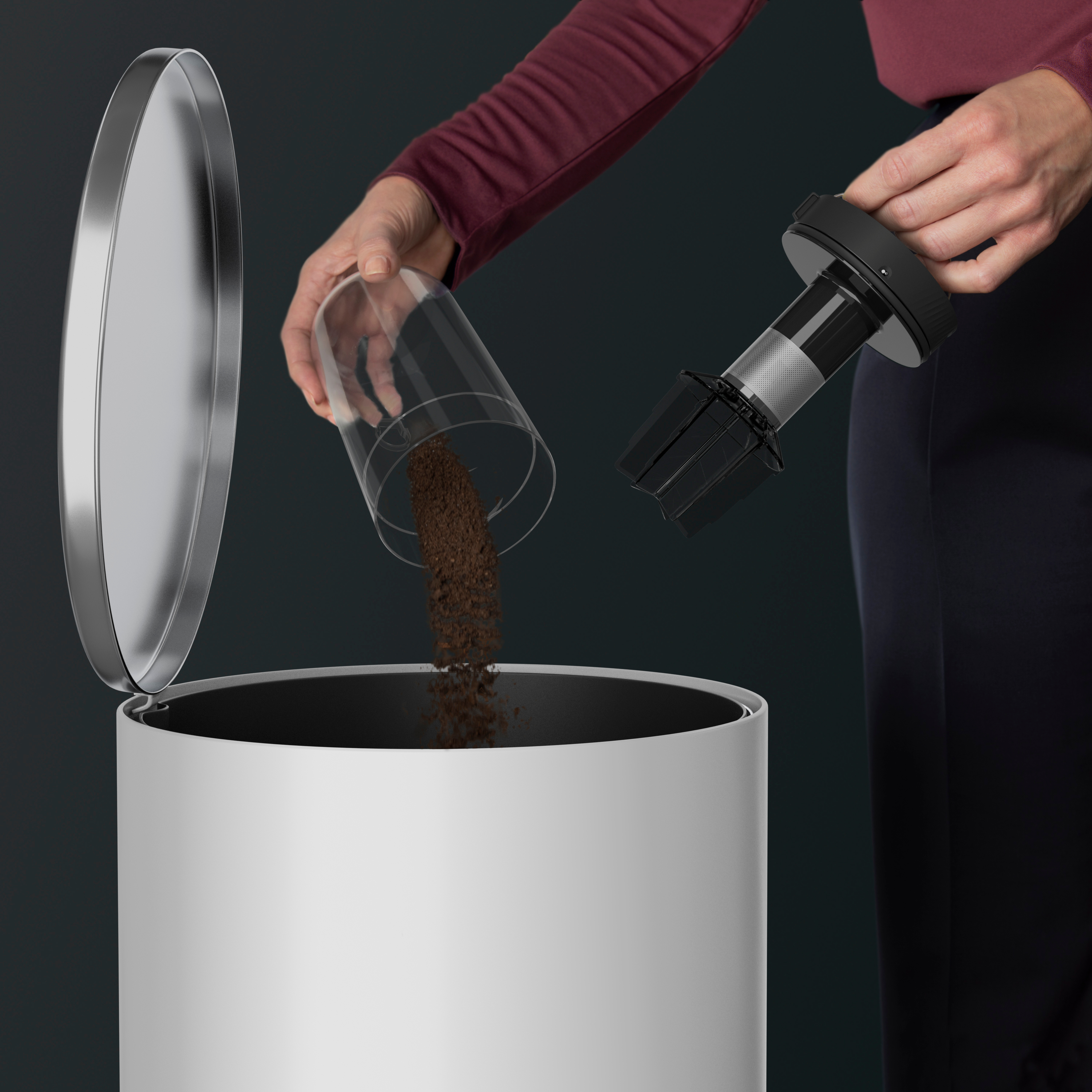 A person emptying a vacuum cleaner container into a white trash can. Dark background.
