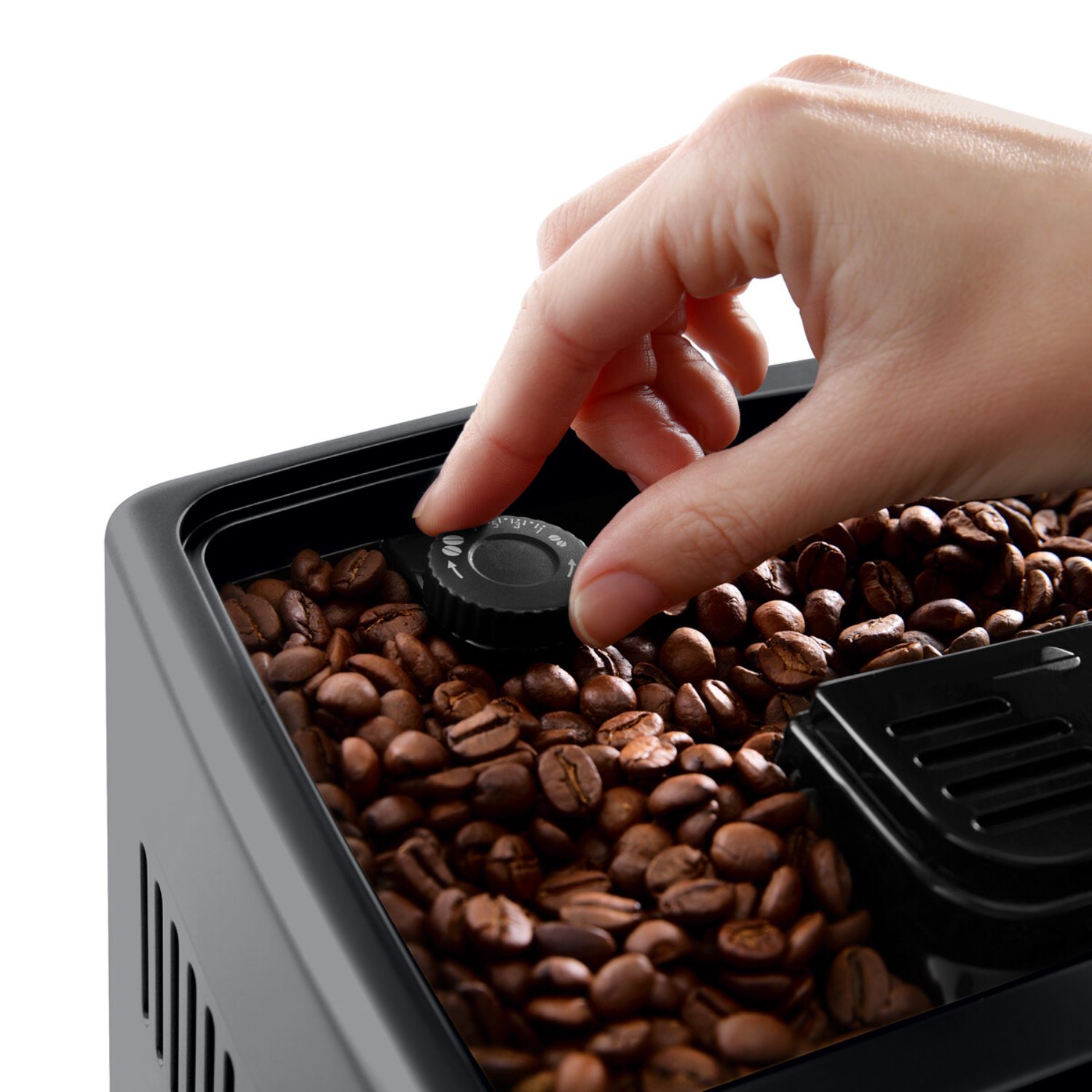 Hand adjusting coffee machine dial, beans in container. Black machine, white background.