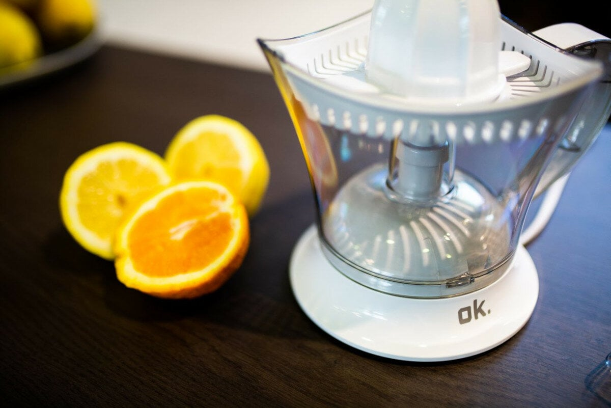 Wyiskarka do cytrusów z cytrynami i połówką pomarańczy na ciemnej powierzchni.