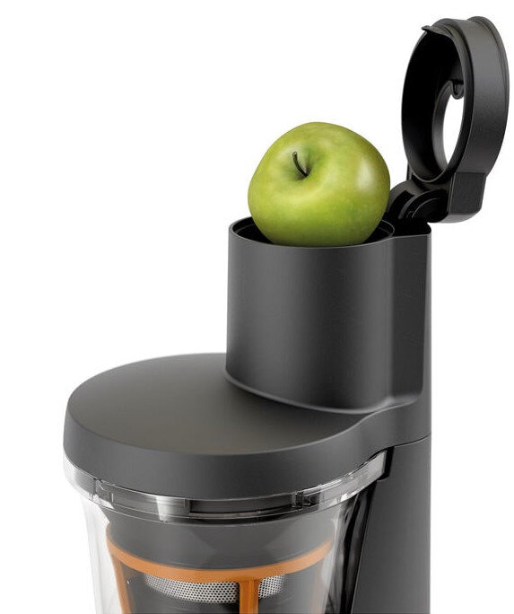 Zielone jabłko w górnej części czarnej wyciskarki do soku, białe tło.