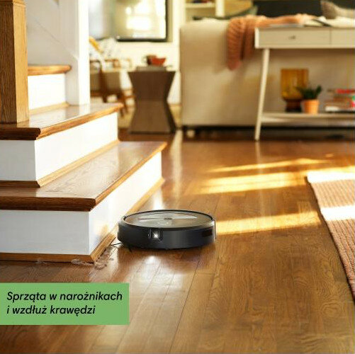 Robot sprzątający odkurza drewnianą podłogę przy schodach, tekst po polsku.