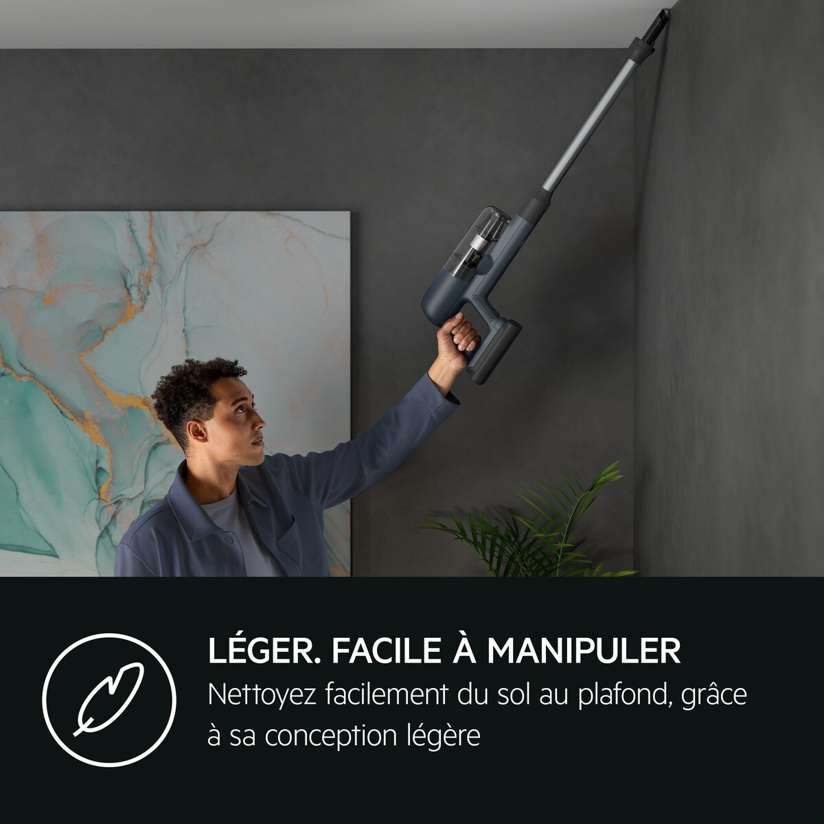 Homme nettoyant un mur avec un aspirateur sans fil gris foncé.