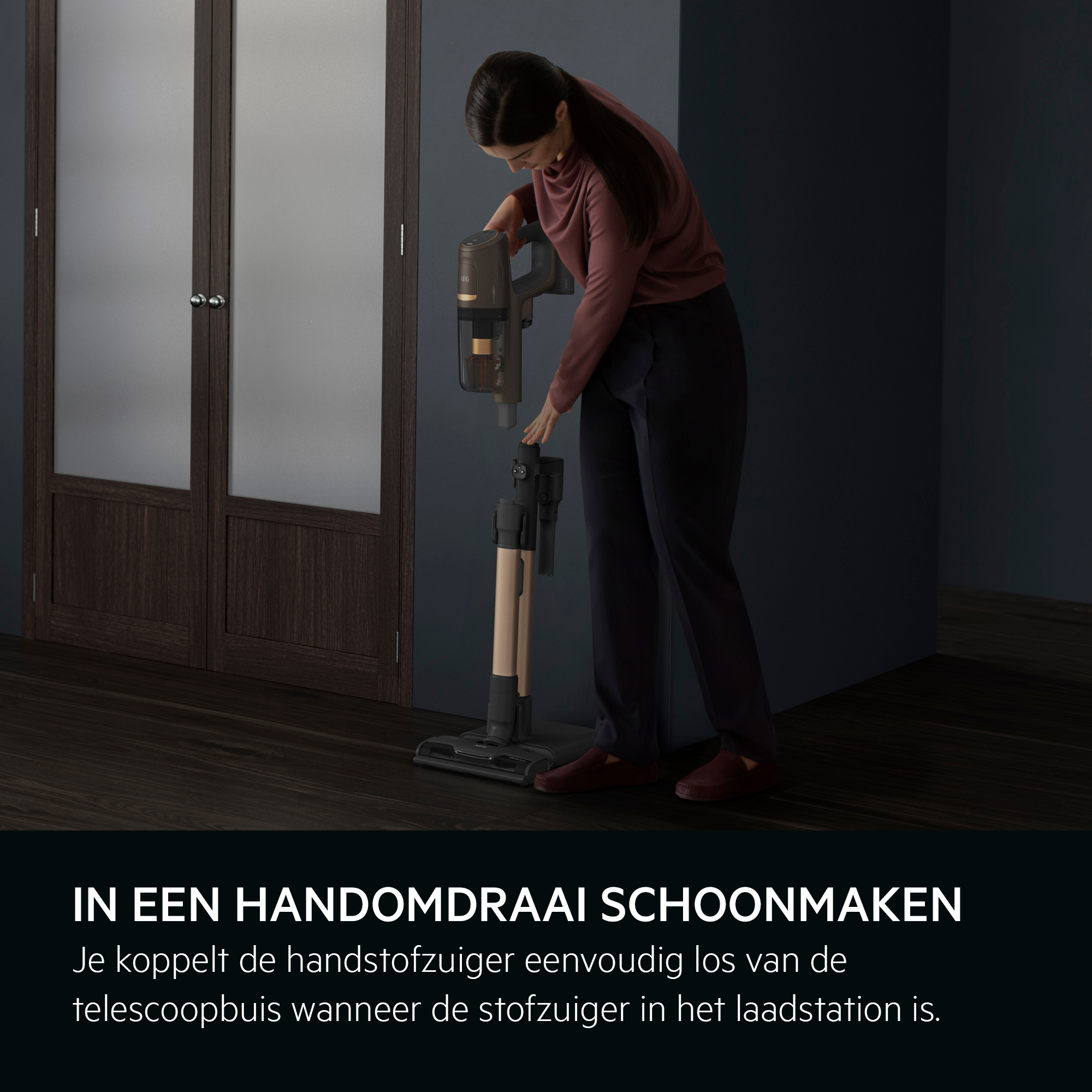 A woman is using a vacuum cleaner in a room. The vacuum cleaner is black and grey. There are doors in the background.
