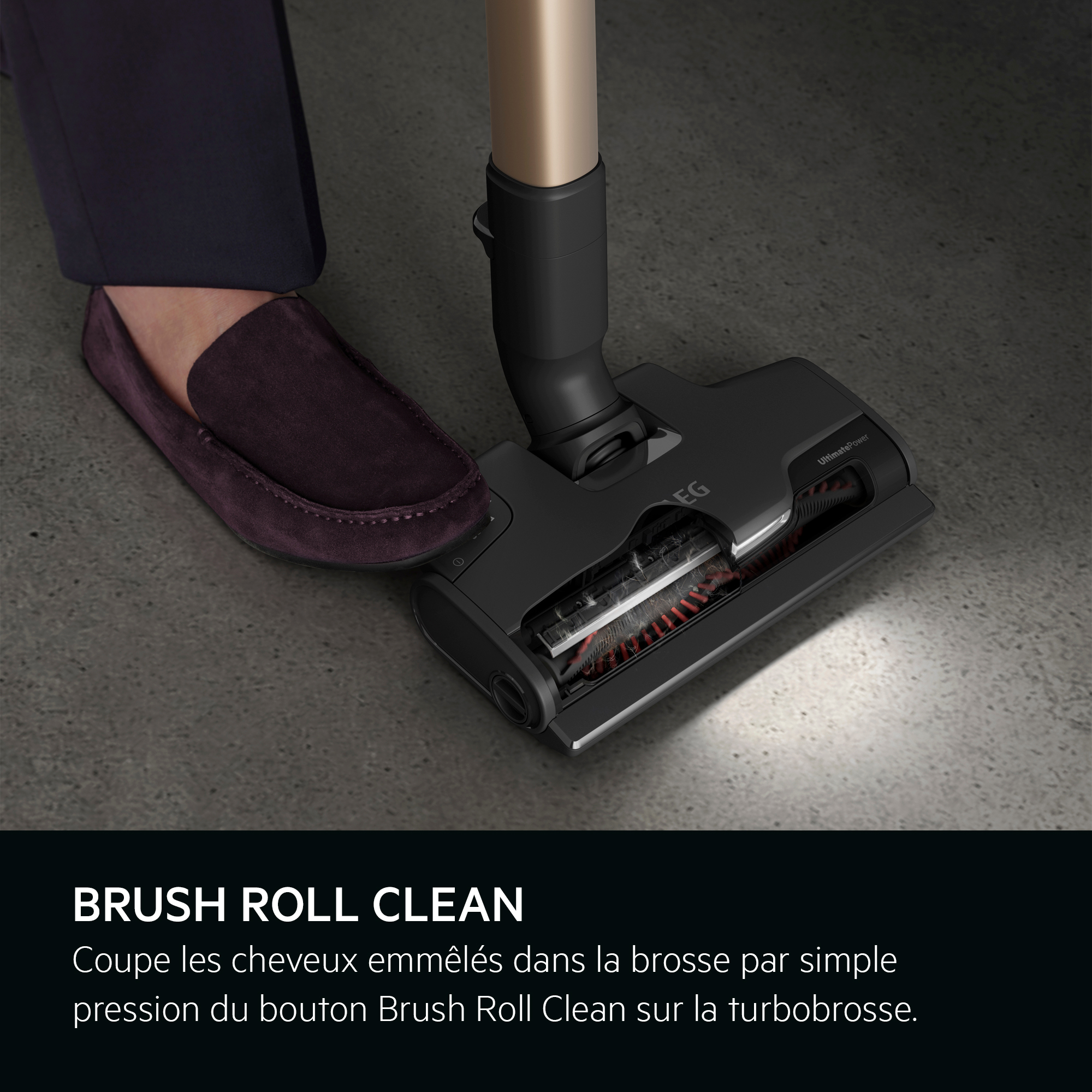 Tête d'aspirateur noire avec texte. La tête est inclinée, montrant le rouleau de brosse. Sol gris.