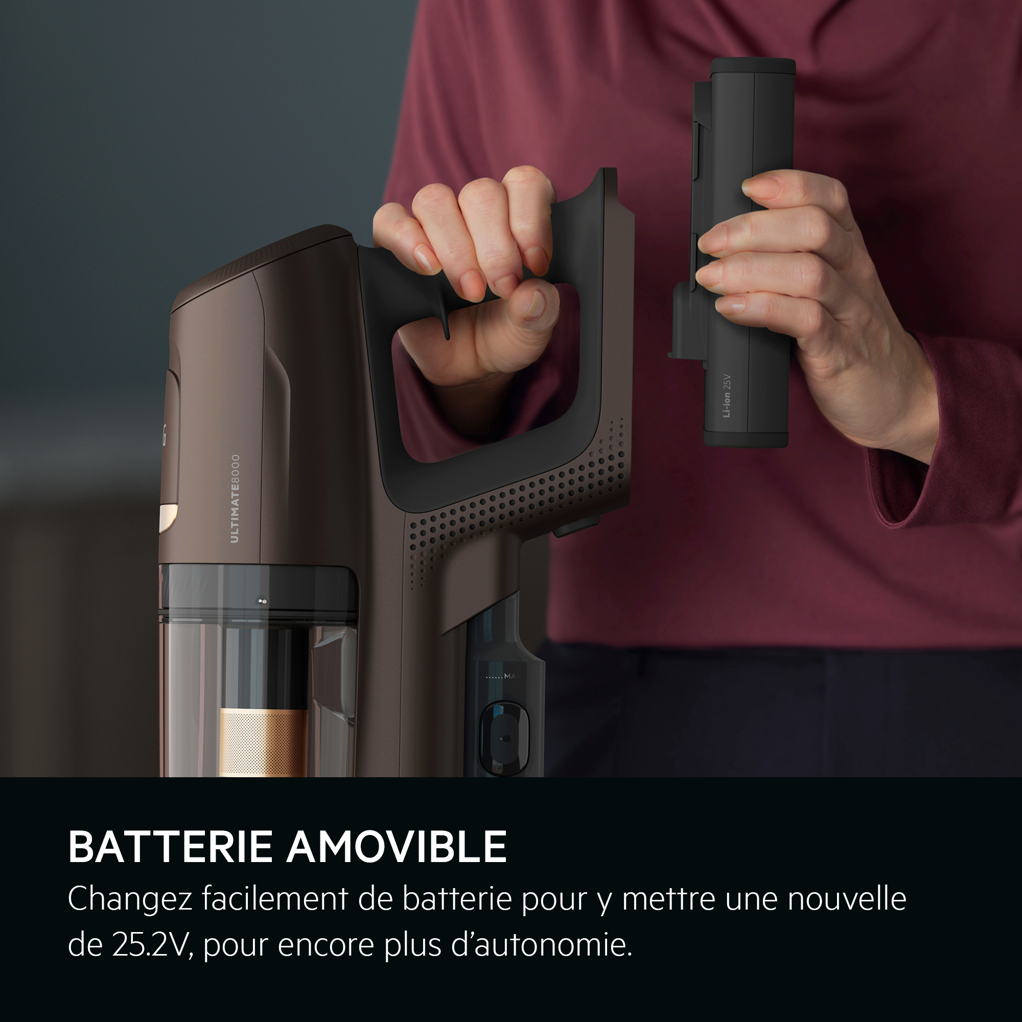 Une personne tenant un aspirateur sans fil et retirant la batterie, de couleur marron.
