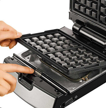 Gofrnica z otwartą górną płytą. Widoczne są dłonie osoby.