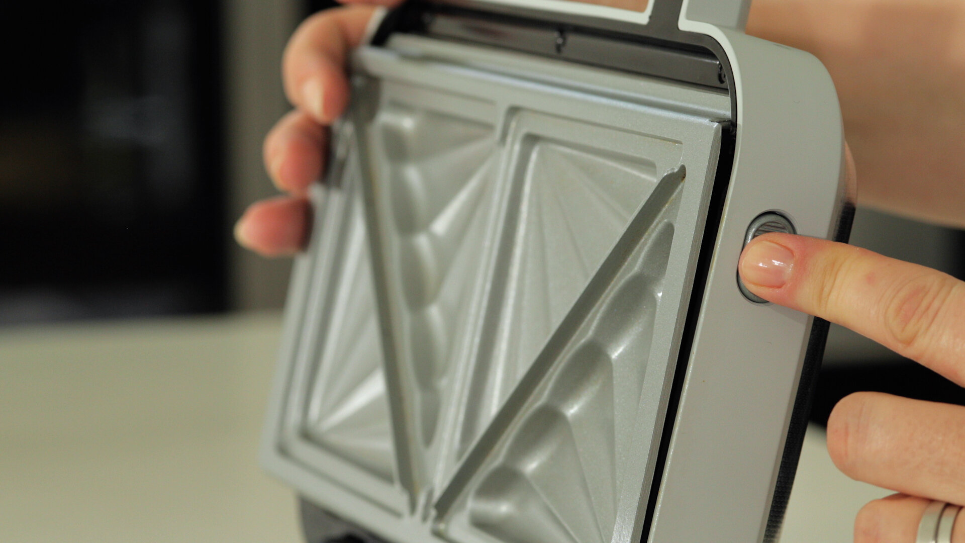 Ręka naciskająca przycisk na srebrnym opiekaczu.