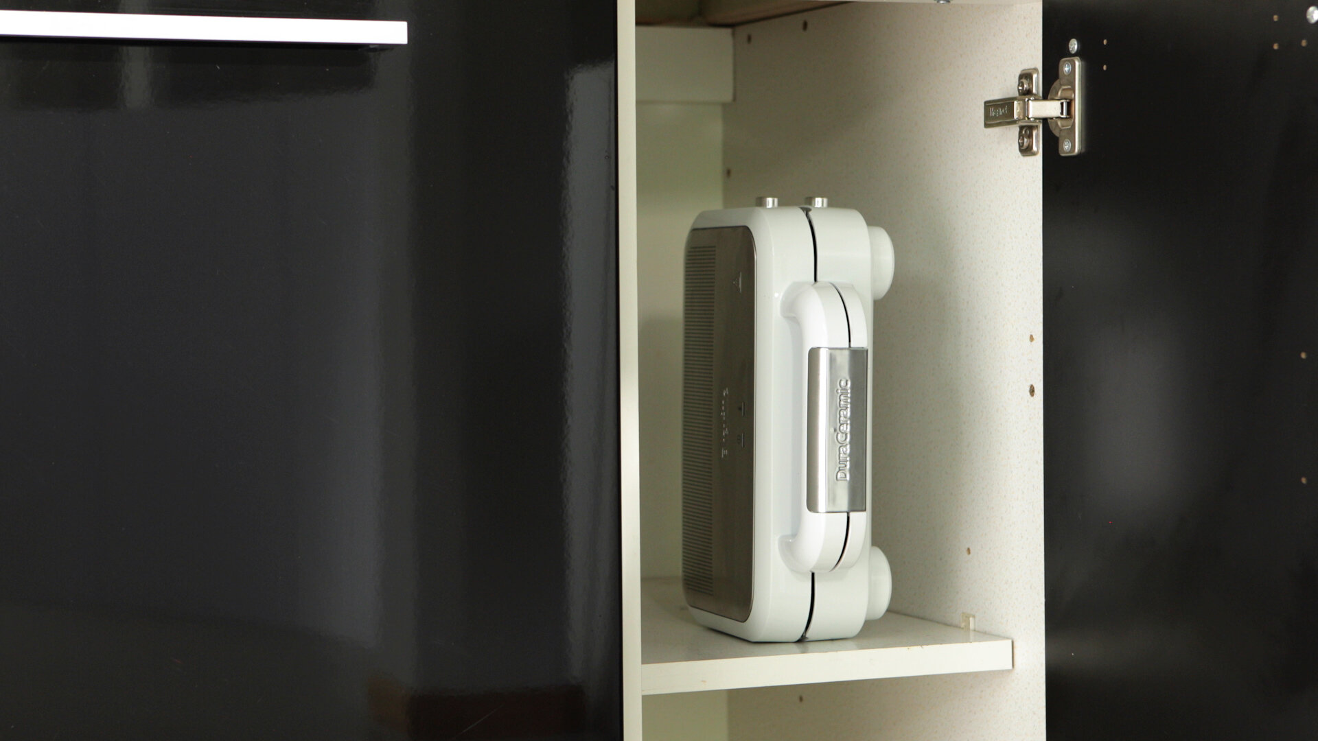 Biały, złożony oczyszczacz powietrza w białej szafce. Czarne boki, biała półka.