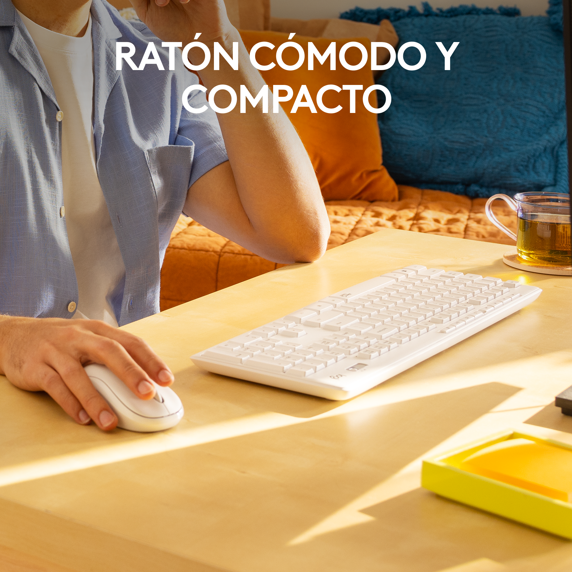 Hombre usando teclado y ratón blancos en un escritorio de madera. Fondo de cojín azul.