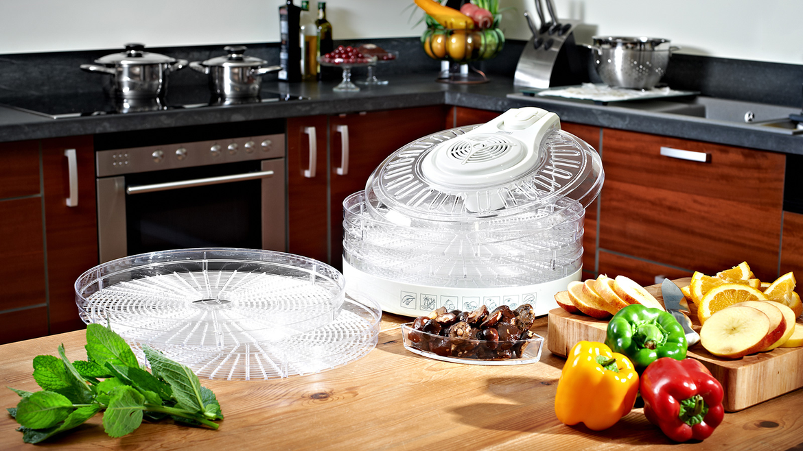 Drewniany stół z suszarką do żywności i różnymi składnikami, takimi jak owoce i warzywa.