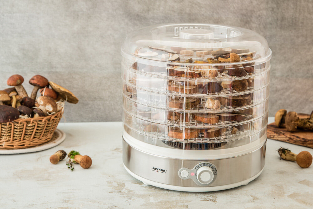 Suszarka do grzybów wypełniona grzybami. Jest kosz grzybów i kilka na drewnianej desce.