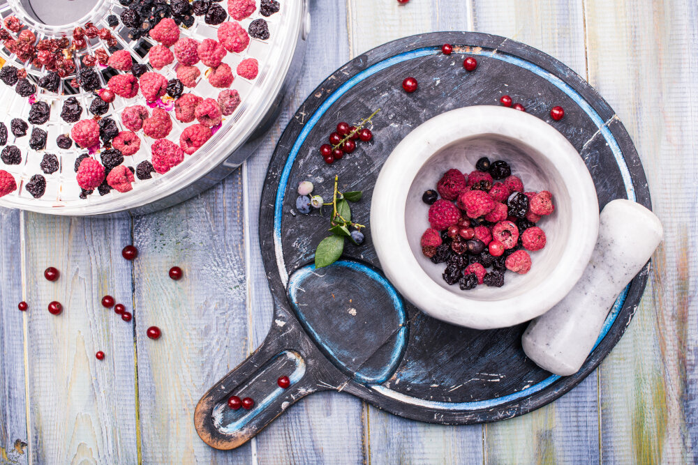 Jagody i suszone owoce na drewnianym stole. Widoczny biały moździerz i tłuczek. Ujęcie z góry.