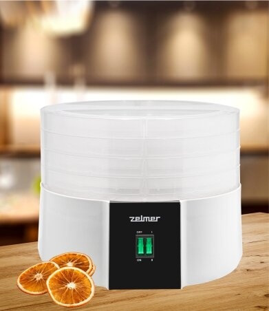 Biała suszarka do żywności ze stosowanymi tacami, plasterkami pomarańczy i czarnym panelem.