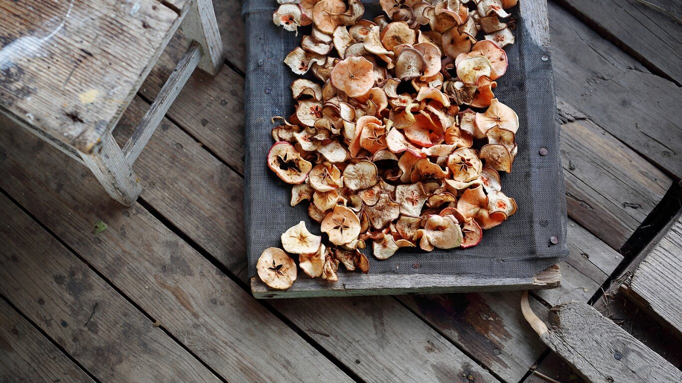 Widok z góry na suszone plasterki jabłek na drewnianym stojaku, na drewnianym pokładzie.