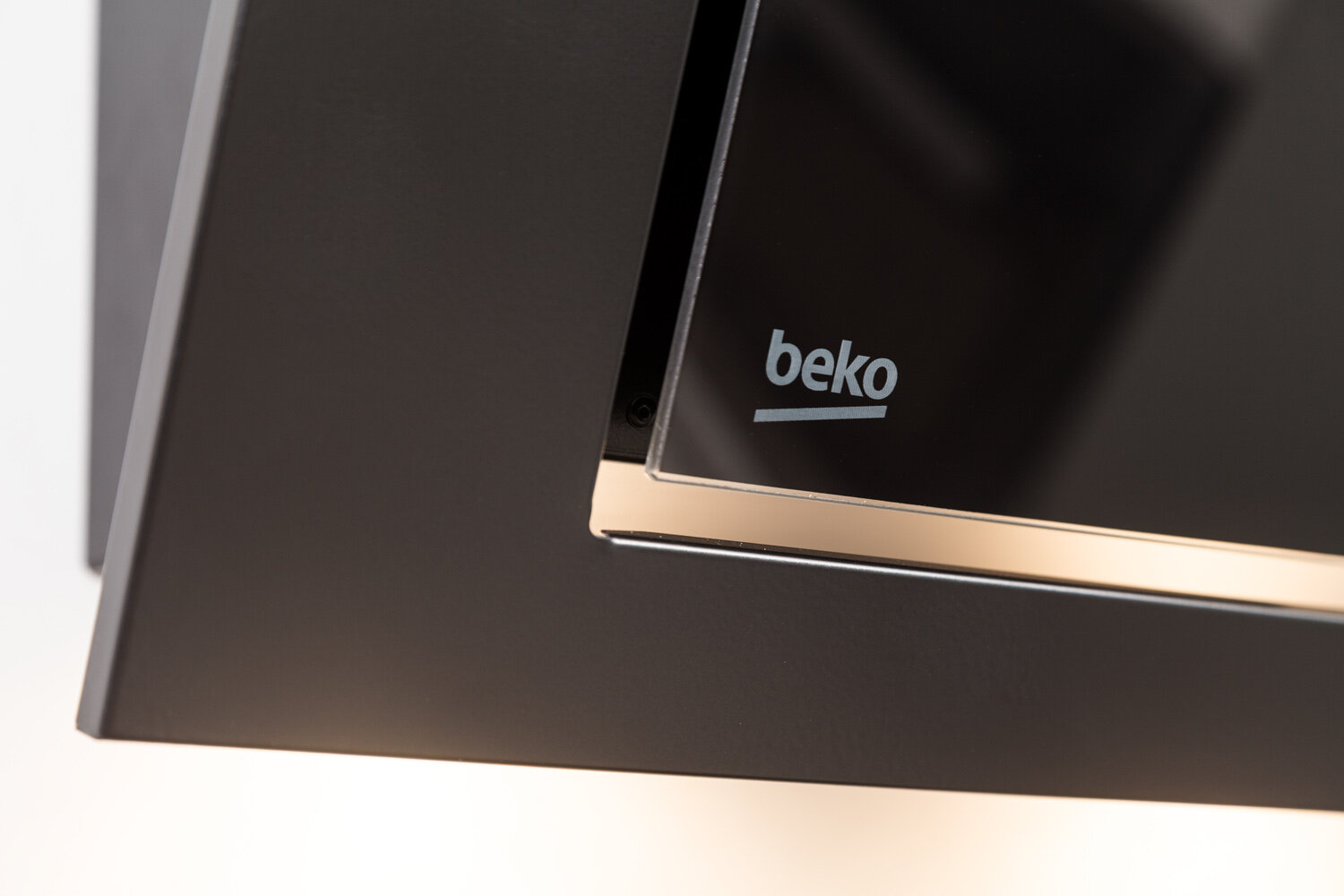 Zbliżenie logo okapu kuchennego na czarnym szkle z metalową ramką.