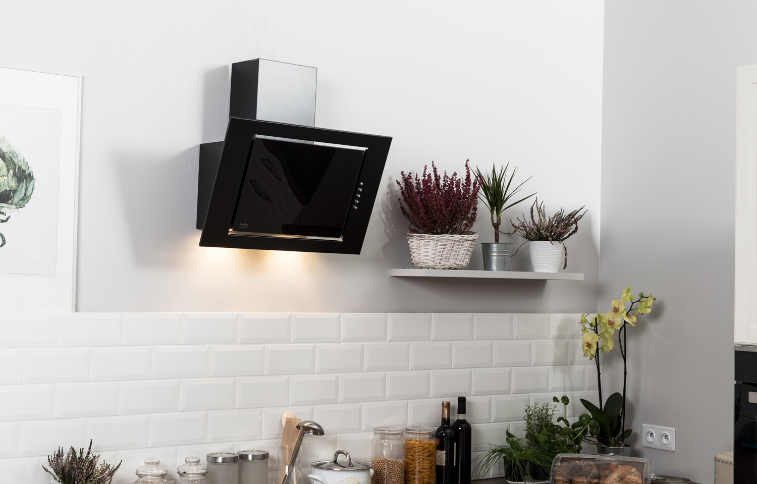 Nowoczesny czarny okap nad białymi płytkami metra, z roślinami na półce.