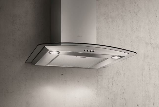 Okap ze stali nierdzewnej ze szklanym frontem jest zamontowany na teksturowanej szarej ścianie. Okap ma światła i przyciski sterowania.