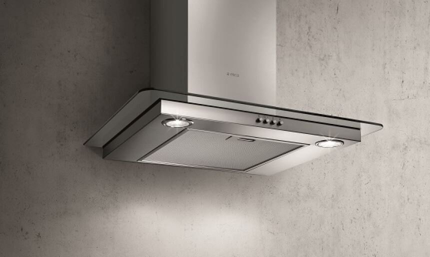 Okap ze stali nierdzewnej ze szklanym panelem, światłami i przyciskami zamontowany na teksturowanej szarej ścianie.