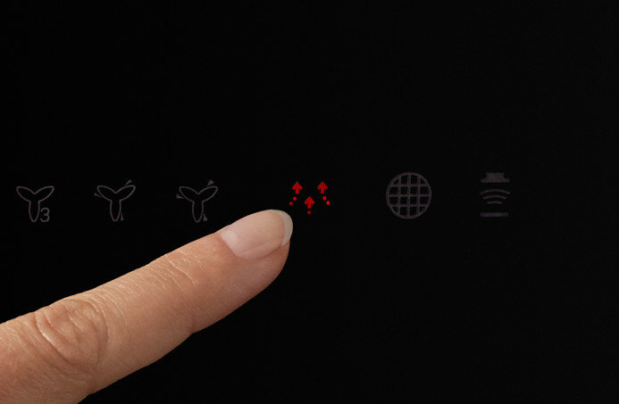 Ręka dotyka czarnej powierzchni z ikonami wentylatorów i strzałek.