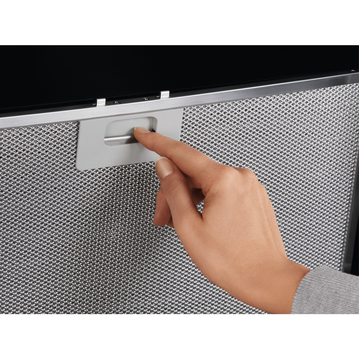 Ręka naciskająca przycisk na metalowym filtrze okapu kuchennego.