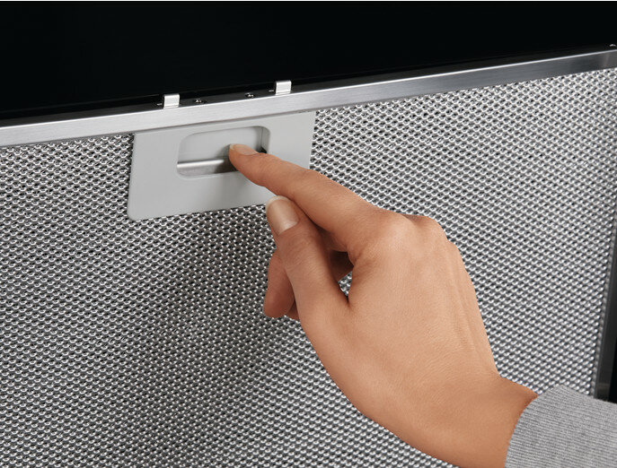 Ręka naciskająca przycisk na metalowym filtrze siatkowym, część urządzenia kuchennego.