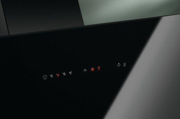 Zbliżenie czarnego panelu sterowania okapu z podświetlanymi czerwonymi ikonami i szklanym panelem.