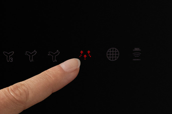 Palec naciskający czerwoną ikonę wentylatora na czarnym panelu.